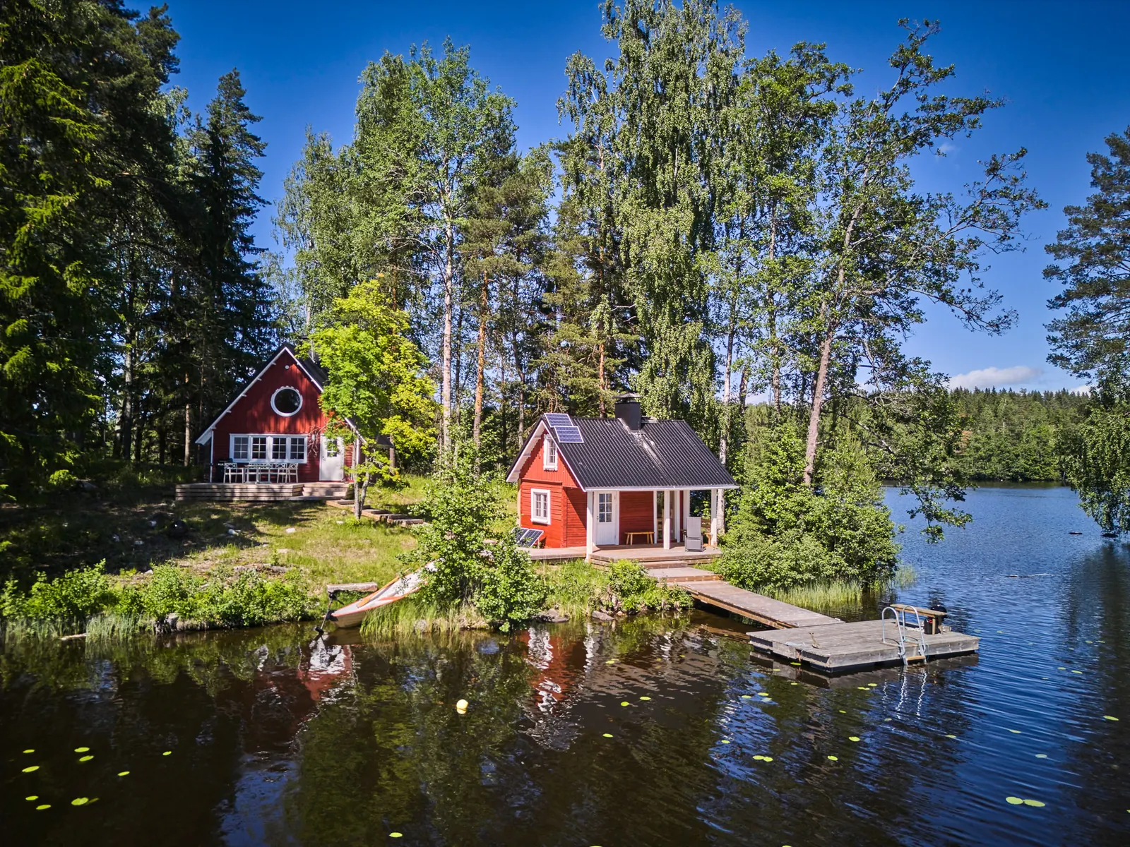 Luftbild: rotes Sommerhaus, Saunahaus und Steg am Ufer der Insel